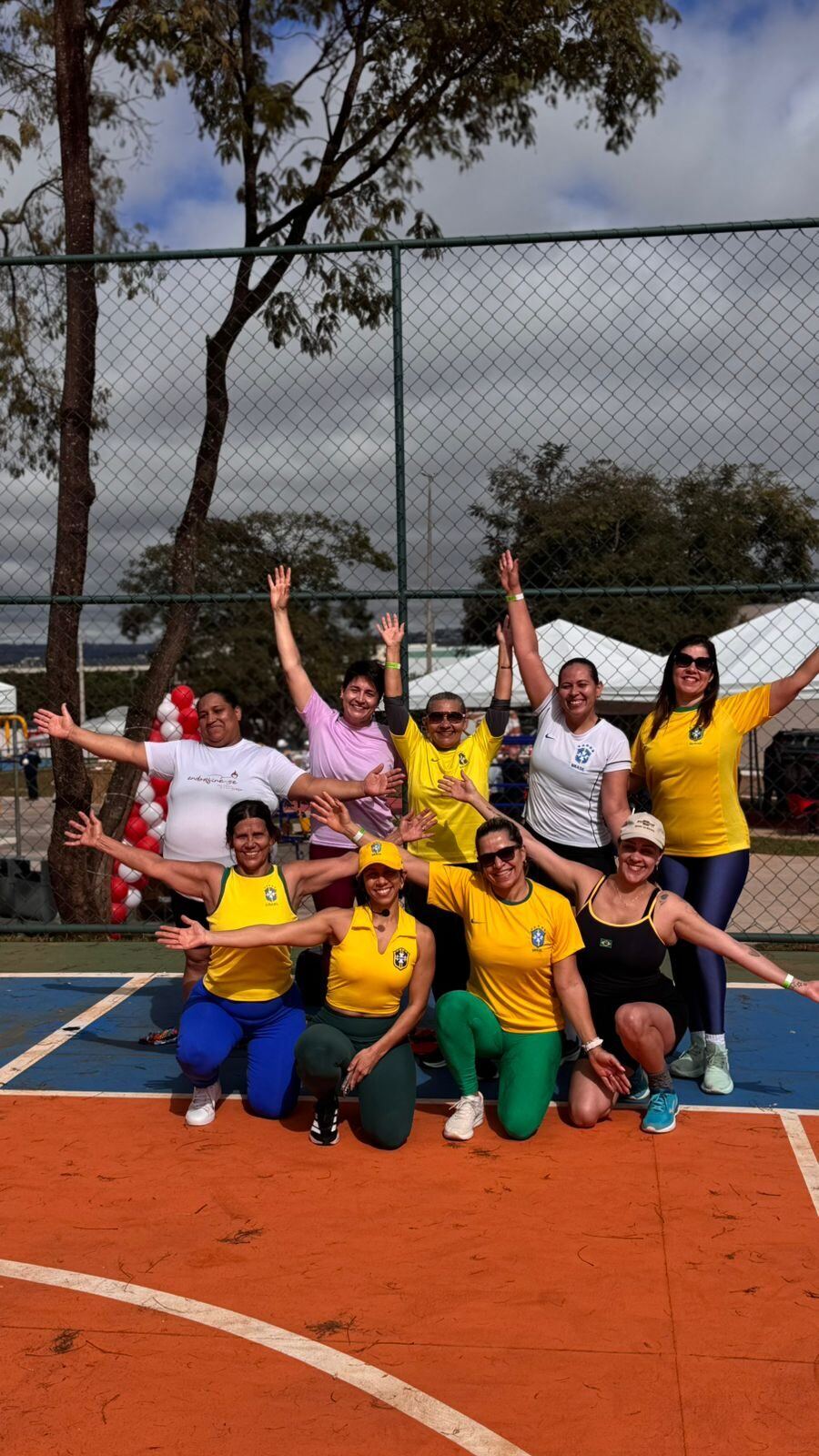 Musas de braços abertos na quadra, vestidas de verde e amarelo, comemorando o fim do treino